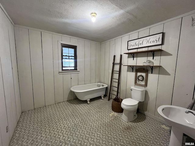 bathroom with sink, wood walls, a textured ceiling, toilet, and a bathtub