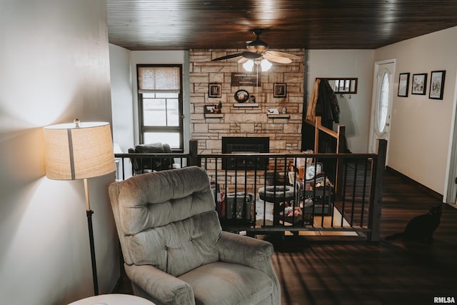 living area with ceiling fan, a stone fireplace, and hardwood / wood-style flooring