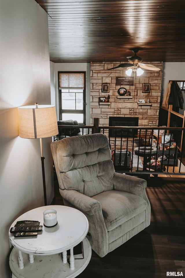 living room featuring ceiling fan, hardwood / wood-style floors, a stone fireplace, and wood ceiling