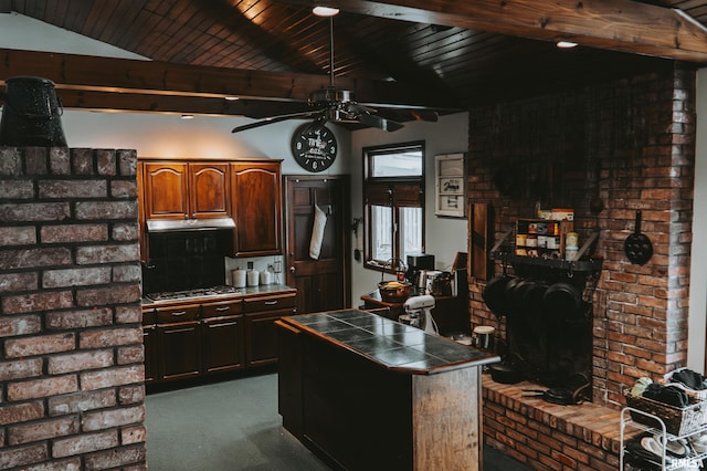 kitchen featuring ceiling fan, light colored carpet, stainless steel gas stovetop, a center island, and tile counters