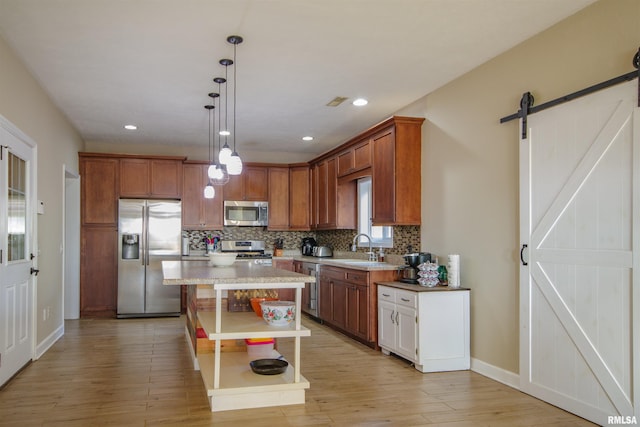 kitchen with light wood-type flooring, appliances with stainless steel finishes, a barn door, and decorative light fixtures