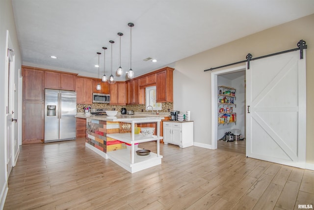 kitchen featuring a barn door, light wood-type flooring, appliances with stainless steel finishes, decorative light fixtures, and a kitchen island