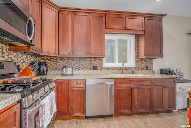 kitchen with light stone countertops, sink, stainless steel appliances, tasteful backsplash, and light wood-type flooring