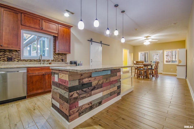 kitchen with backsplash, hanging light fixtures, stainless steel dishwasher, a barn door, and light hardwood / wood-style floors