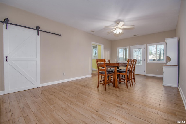 dining area with a barn door, ceiling fan, and light wood-type flooring