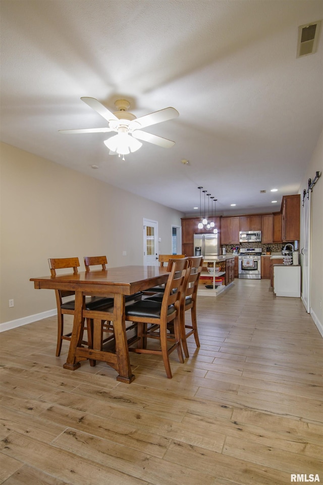 dining area with ceiling fan, a barn door, and light wood-type flooring