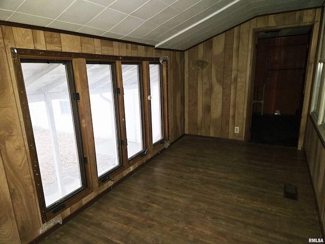 empty room featuring lofted ceiling, dark wood-type flooring, and wooden walls