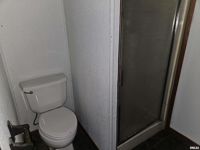 bathroom featuring tile patterned floors, toilet, and a shower with shower door