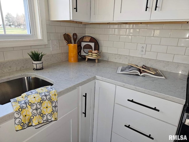 kitchen featuring decorative backsplash, light stone countertops, and white cabinets