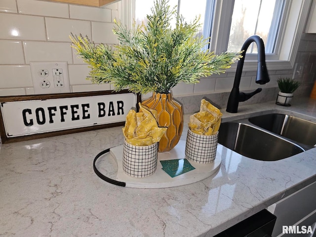 interior details featuring a sink, decorative backsplash, and light stone counters