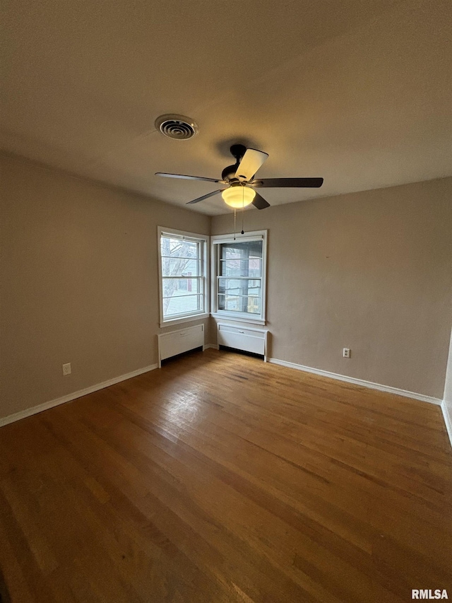 empty room with hardwood / wood-style floors, ceiling fan, and radiator heating unit