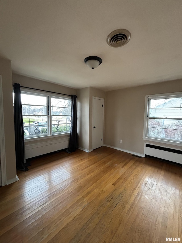 unfurnished room featuring light wood-type flooring, a wealth of natural light, and a baseboard heating unit