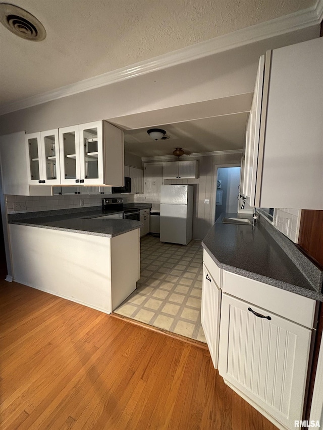 kitchen with light wood-type flooring, backsplash, white refrigerator, white cabinets, and stainless steel range with electric cooktop