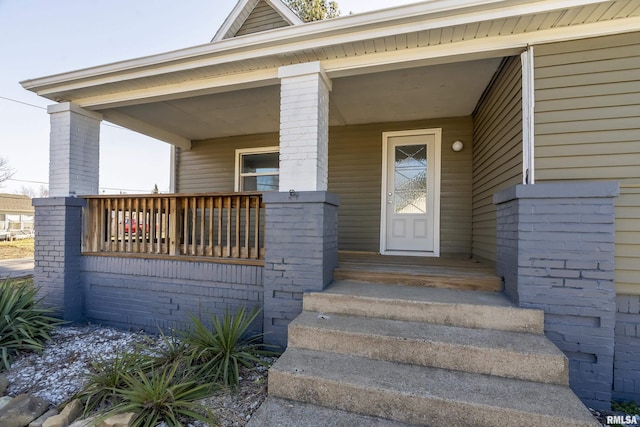 doorway to property with a porch and brick siding