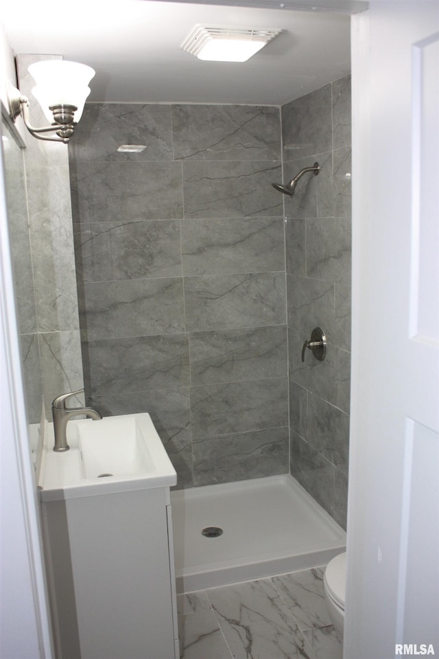 bathroom featuring a tile shower, vanity, and toilet