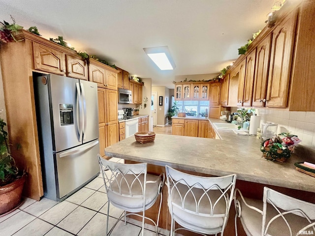 kitchen with sink, light tile patterned floors, appliances with stainless steel finishes, kitchen peninsula, and a breakfast bar area