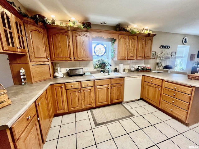 kitchen featuring dishwasher, sink, kitchen peninsula, decorative backsplash, and light tile patterned floors