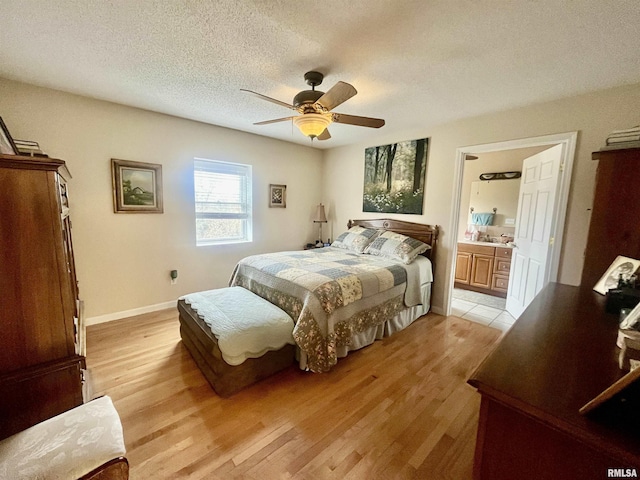 bedroom with ceiling fan, light hardwood / wood-style floors, a textured ceiling, and ensuite bath