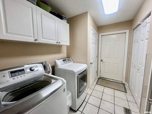 washroom with cabinets, light tile patterned floors, a textured ceiling, and washing machine and clothes dryer