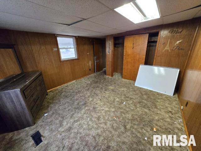 basement featuring carpet flooring, a drop ceiling, and wood walls