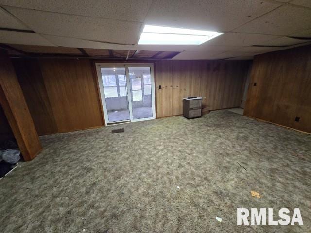 basement with a paneled ceiling, carpet floors, and wood walls