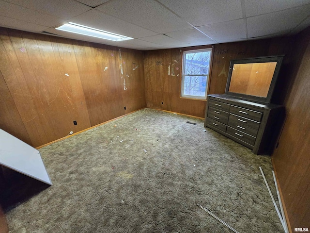 basement with carpet, a drop ceiling, and wooden walls