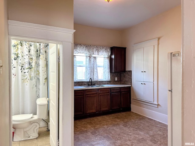 kitchen with a sink, light countertops, dark brown cabinets, backsplash, and freestanding refrigerator