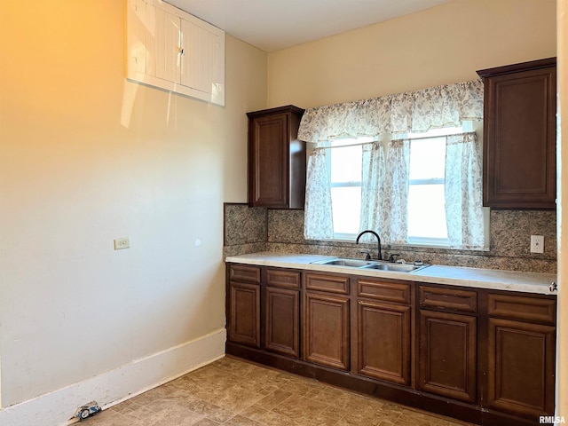 kitchen with light countertops, backsplash, a sink, and baseboards