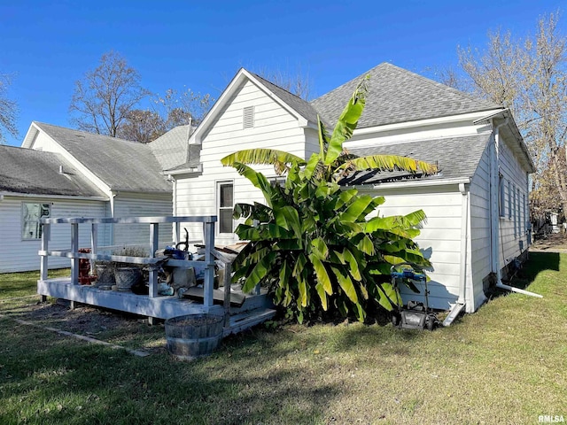 rear view of property with roof with shingles, a deck, and a yard