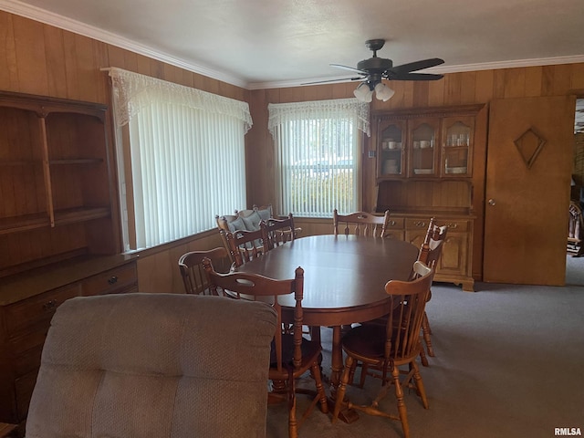 dining area featuring ceiling fan, crown molding, carpet floors, and wood walls