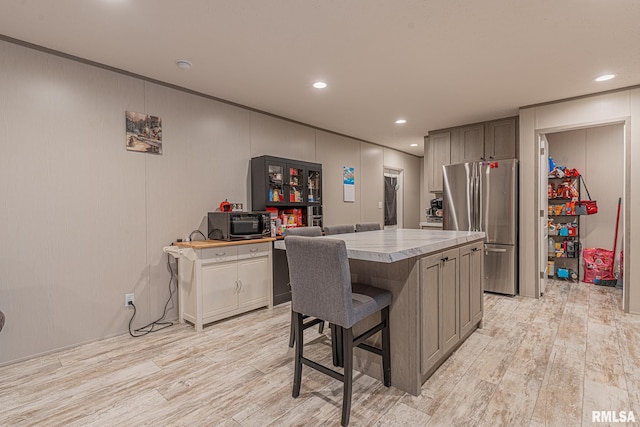 kitchen with stainless steel refrigerator, a center island, light hardwood / wood-style floors, a kitchen bar, and gray cabinets