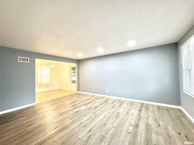 spare room with a notable chandelier, light hardwood / wood-style floors, and a healthy amount of sunlight