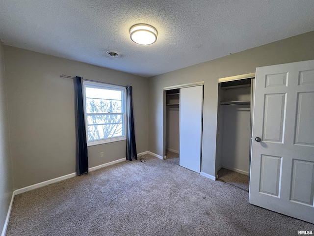 unfurnished bedroom with multiple closets, light carpet, and a textured ceiling