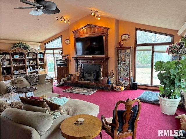 carpeted living room featuring plenty of natural light, ceiling fan, a wood stove, and vaulted ceiling