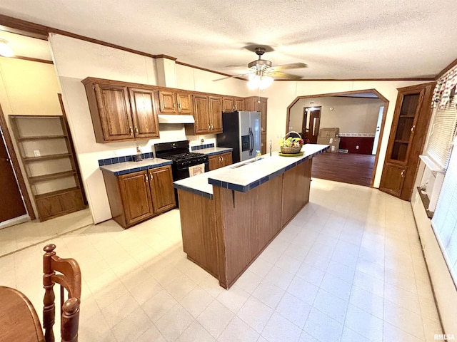 kitchen featuring ceiling fan, tile counters, a center island, black gas range oven, and stainless steel refrigerator with ice dispenser