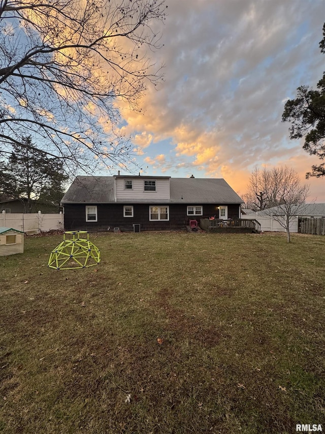 back house at dusk featuring a lawn and a wooden deck