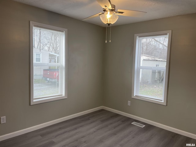 empty room with ceiling fan, dark wood-type flooring, a healthy amount of sunlight, and a textured ceiling