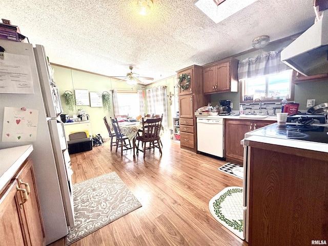 kitchen with light wood finished floors, range hood, plenty of natural light, white appliances, and a sink