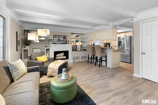 living room featuring beamed ceiling, light wood-type flooring, a brick fireplace, and ornamental molding