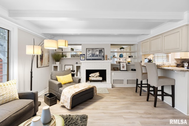 living room featuring beam ceiling, light wood-type flooring, crown molding, and a brick fireplace