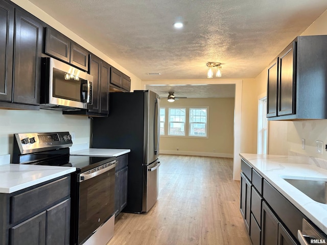 kitchen with light hardwood / wood-style flooring, ceiling fan, a textured ceiling, appliances with stainless steel finishes, and light stone counters