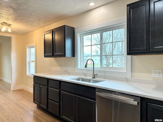 kitchen with sink, stainless steel dishwasher, light wood-type flooring, a textured ceiling, and light stone counters