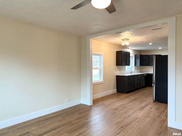 kitchen featuring light wood-type flooring, a textured ceiling, ceiling fan, sink, and stainless steel refrigerator