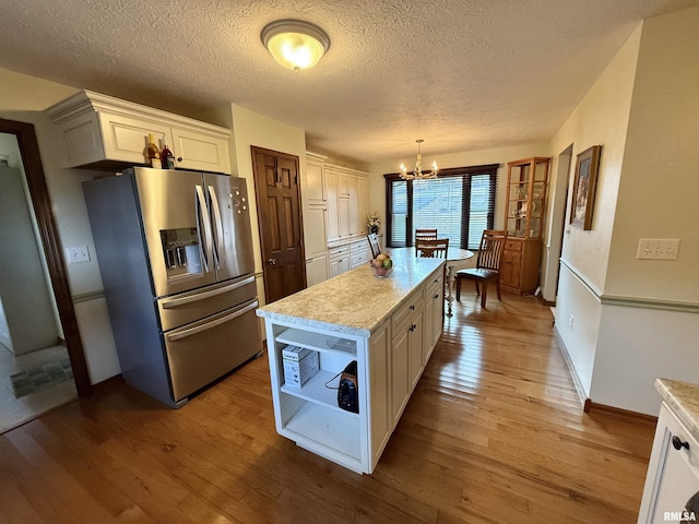 kitchen with stainless steel refrigerator with ice dispenser, decorative light fixtures, white cabinetry, and a notable chandelier