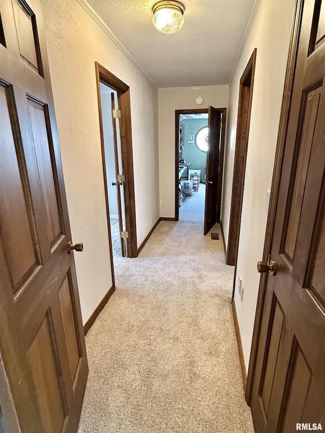 corridor featuring a textured ceiling, crown molding, and light carpet