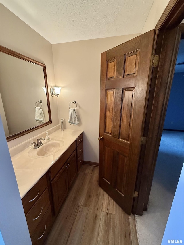 bathroom featuring vaulted ceiling, vanity, wood-type flooring, and a textured ceiling