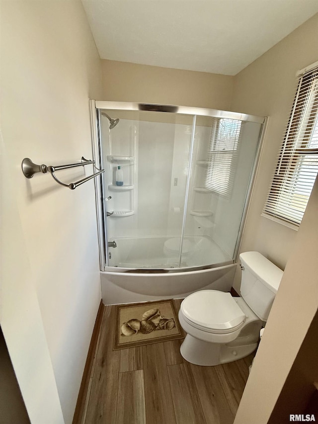 bathroom with toilet, wood-type flooring, and bath / shower combo with glass door