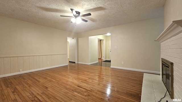 unfurnished living room with a textured ceiling, ceiling fan, dark hardwood / wood-style floors, and a brick fireplace