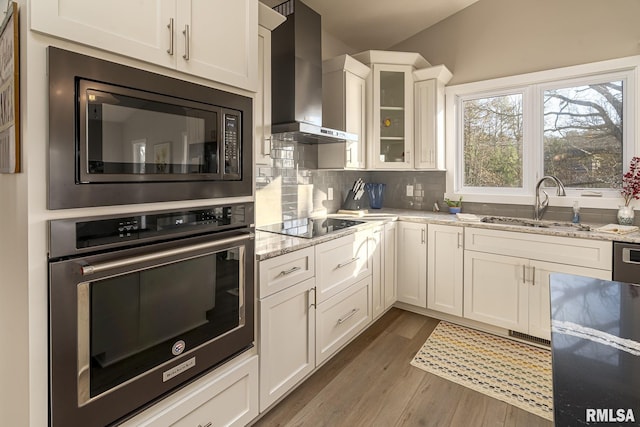 kitchen with wall chimney exhaust hood, built in microwave, oven, and light stone countertops