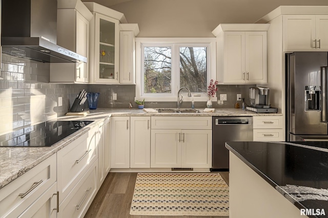 kitchen featuring light stone countertops, appliances with stainless steel finishes, sink, wall chimney range hood, and white cabinetry